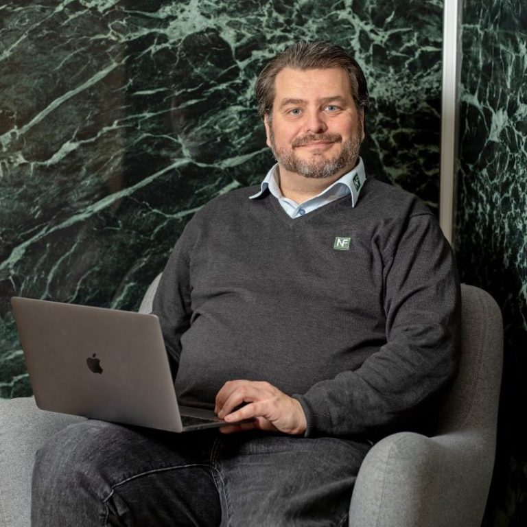 Medarbejder med bærbar computer foran en grøn stenvæg